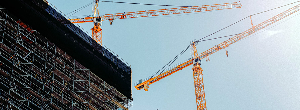 Two construction cranes next to a building that is in process of being built.