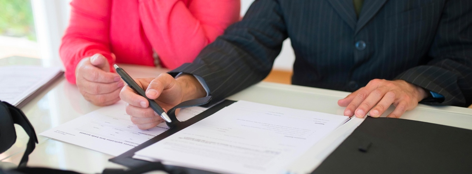 A man in a business suit, holding a pen above a stack of papers.