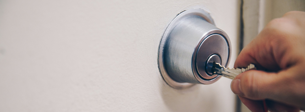 A hand putting a key into the deadbolt of a door to unlock it.